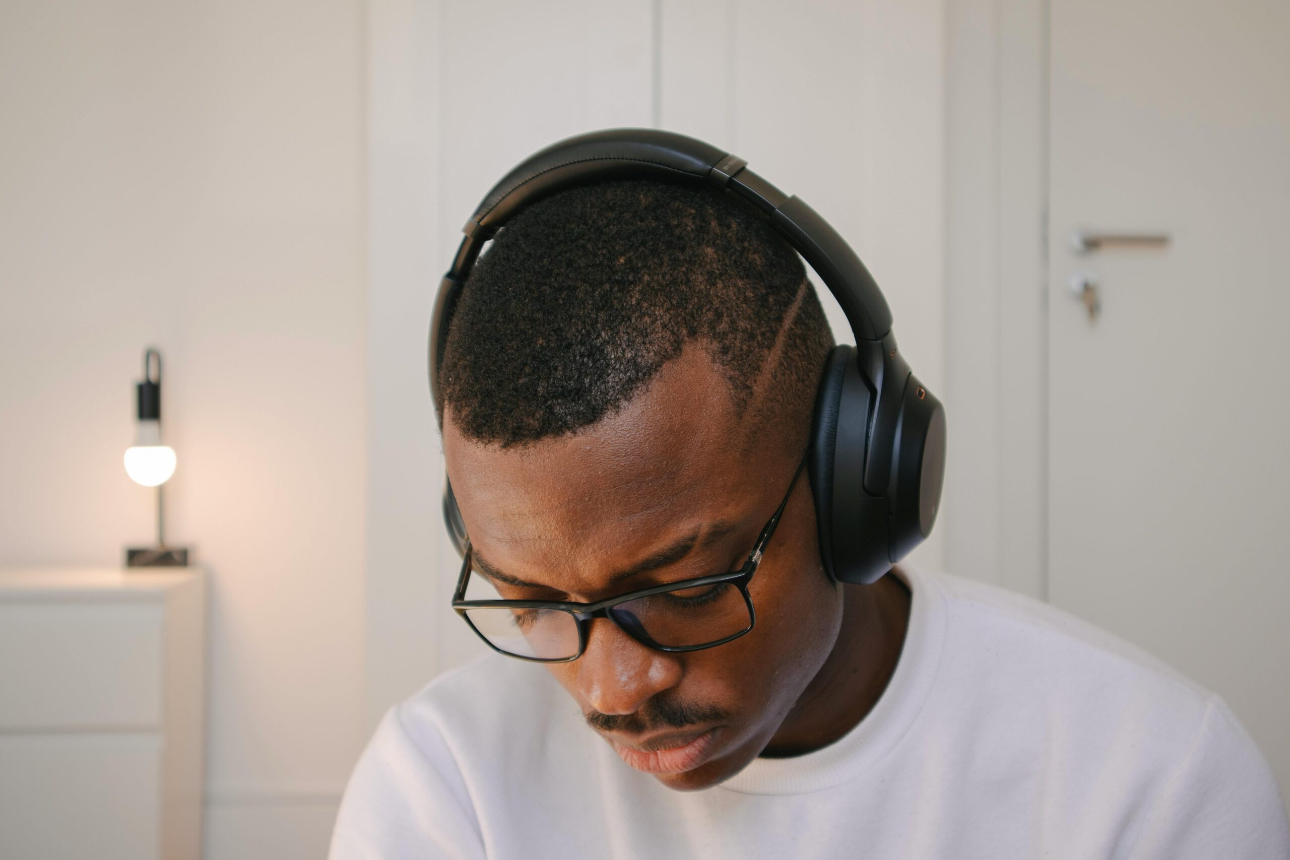 A man wearing headphones and glasses, concentrating in a minimalistic indoor setting, perfect for work or technology themes.
